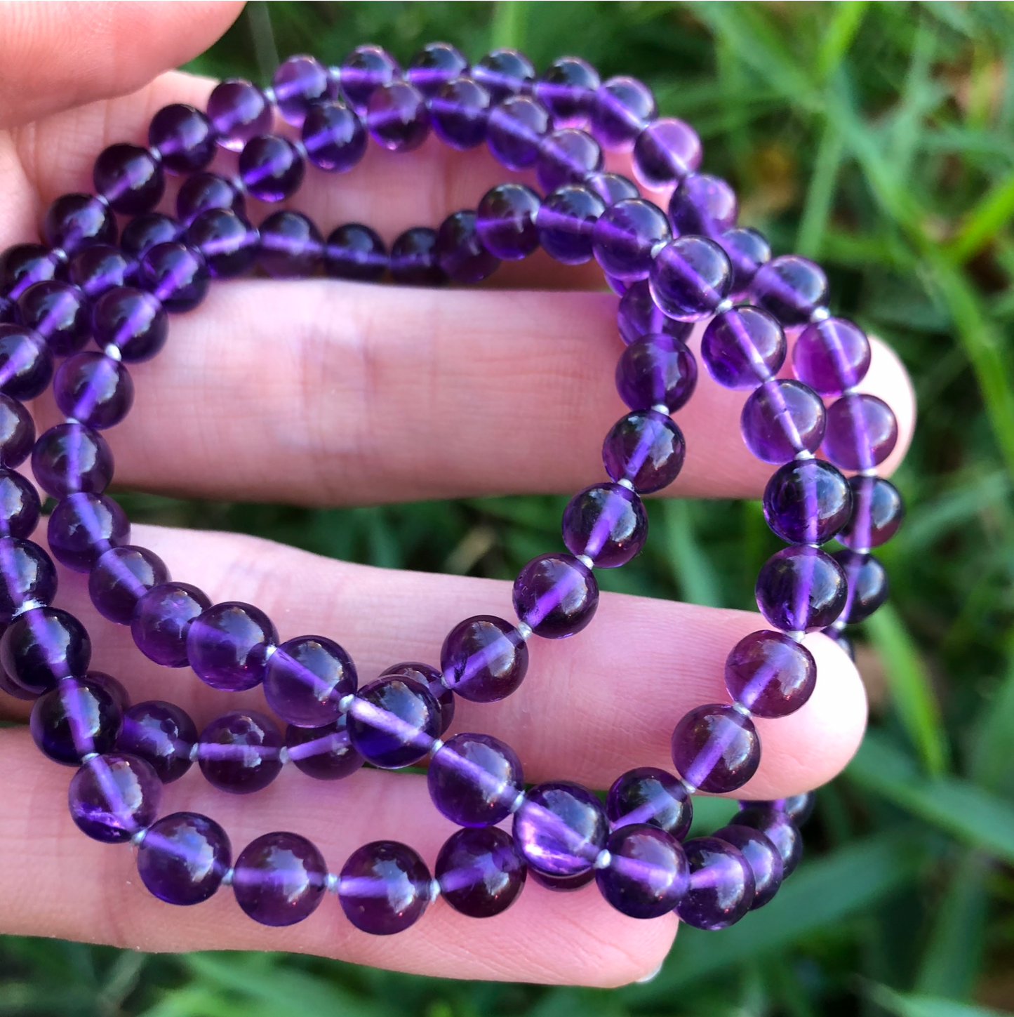 A hand holding a crystal healing Amethyst necklace known for attaining wisdom