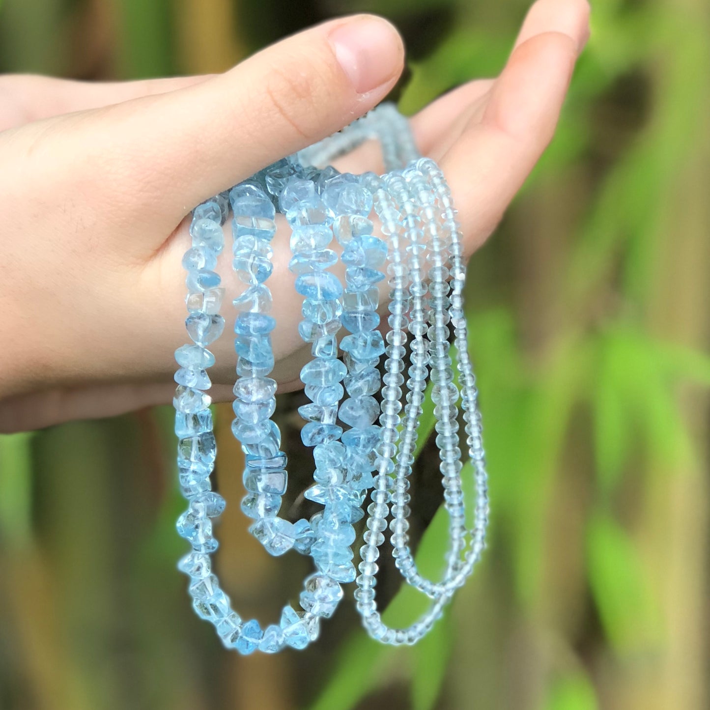 Hands holding two crystal healing Aquamarine necklaces known for heightening your awareness of truth