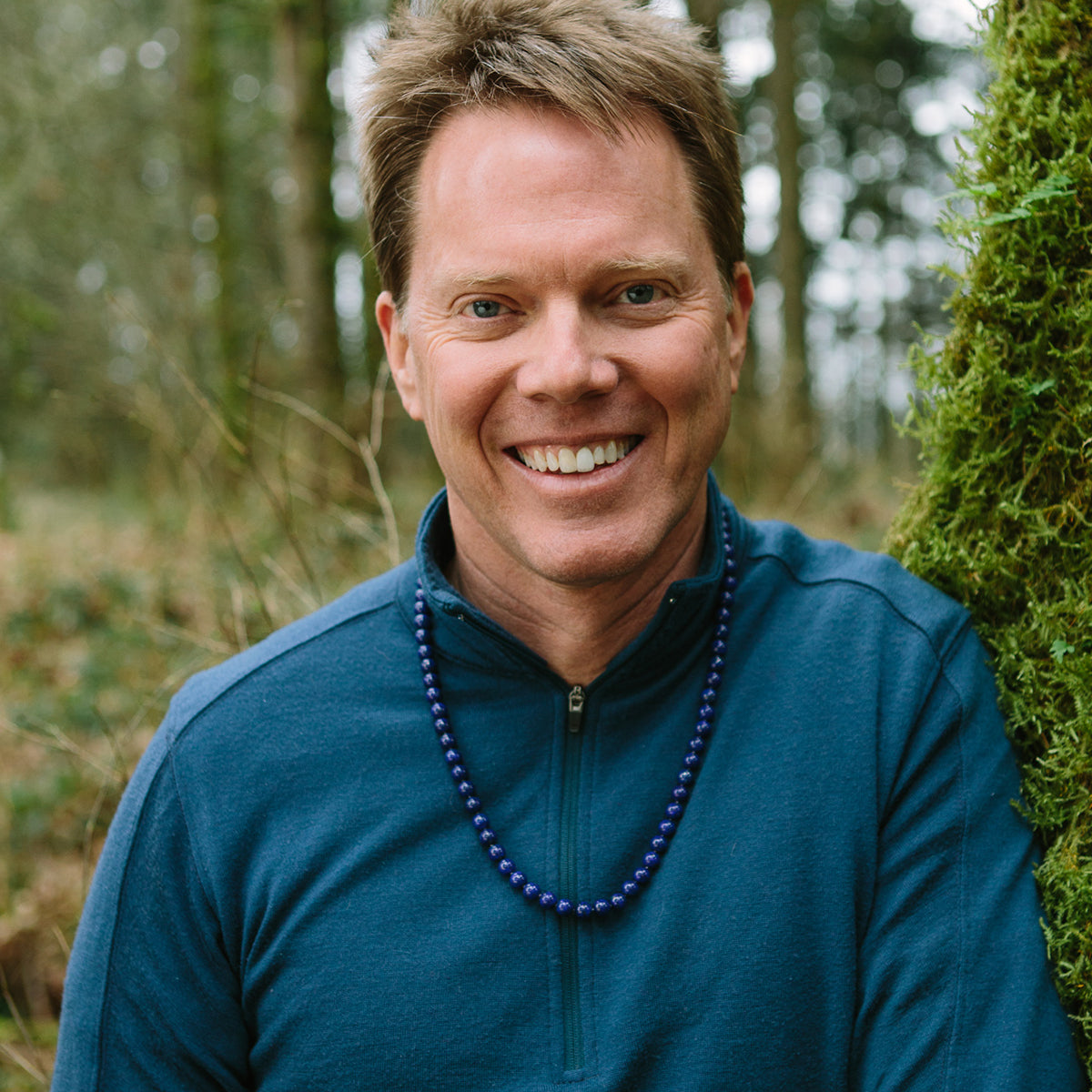 A man smiling in a forest wearing a Crystal healing Lapis Lazuli necklace for harmonizing heart and mind 
