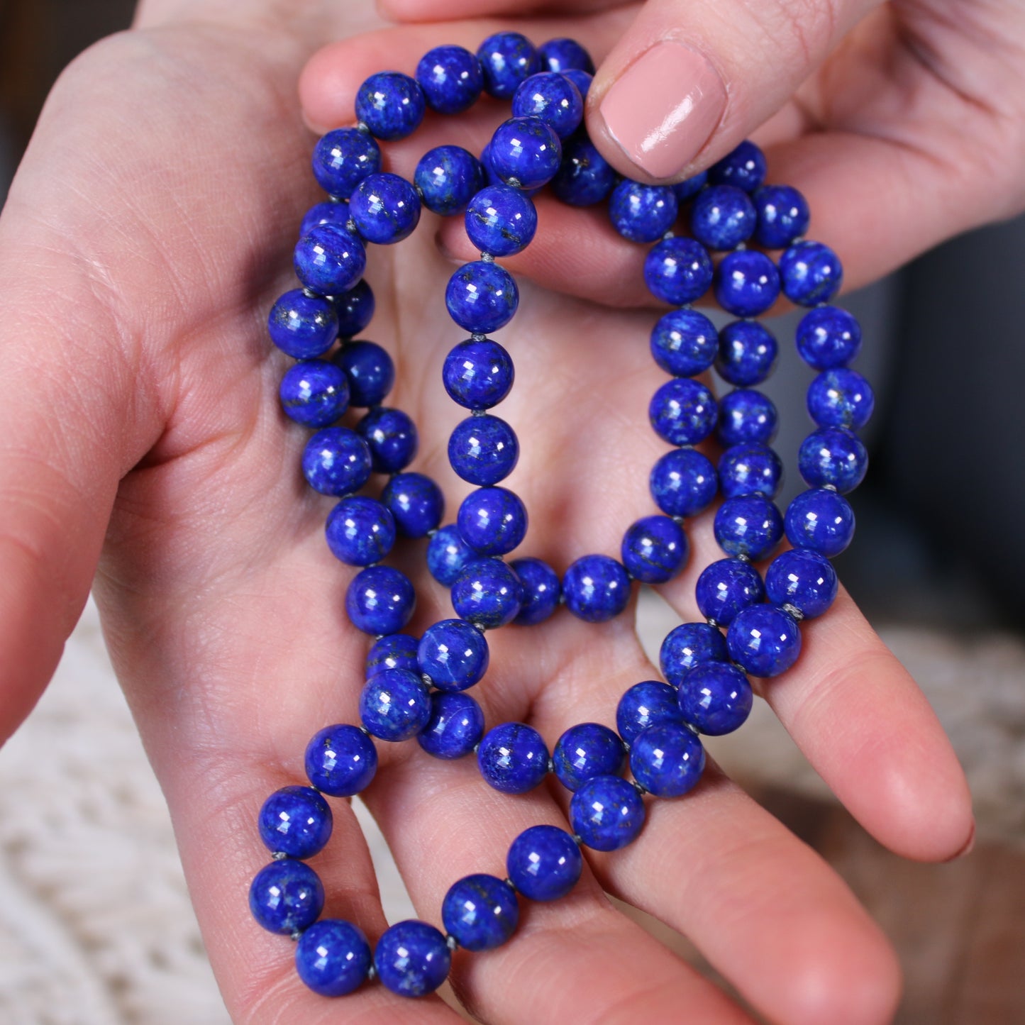 A hand holding a deep blue Crystal healing Lapis Lazuli necklace for harmonizing heart and mind 