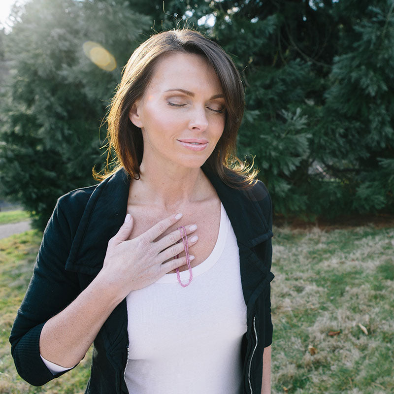 A woman holding a crystal healing Pink Sapphire necklace known for helping heal emotional wounds