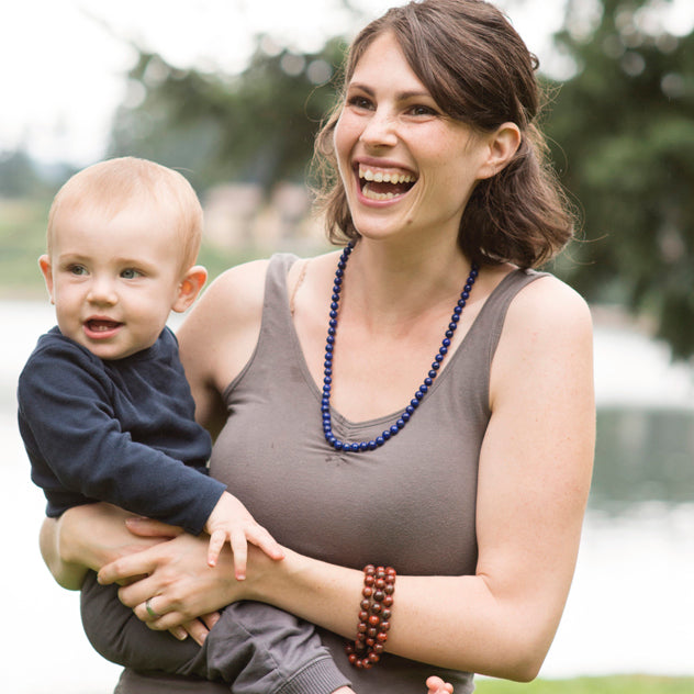A woman holding a baby is smiling and wearing a Crystal healing Lapis Lazuli necklace for harmonizing heart and mind 