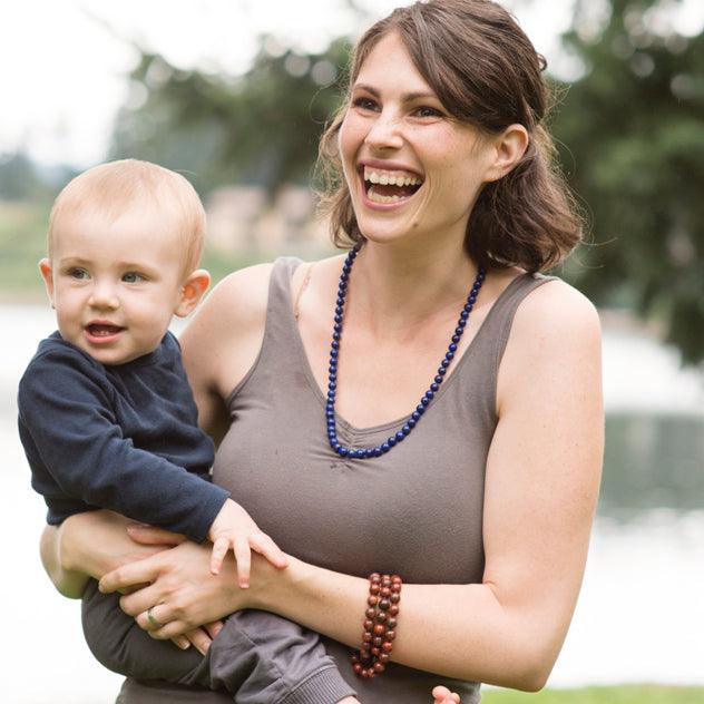 A woman holding a baby is smiling and wearing a Crystal healing Lapis Lazuli necklace for harmonizing heart and mind
