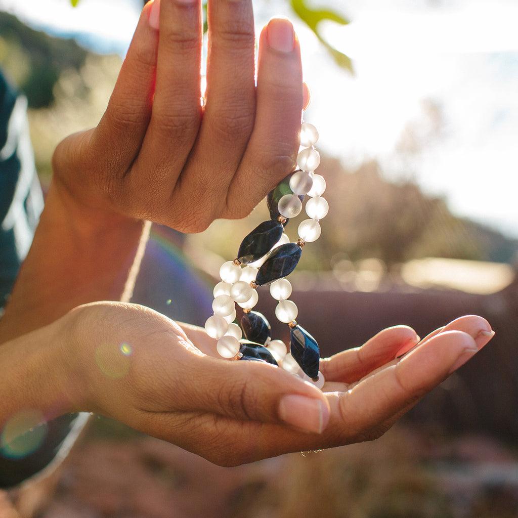 Two hands holding a crystal healing Blue Phoenix necklace known for letting go of limiting habits and attitudes