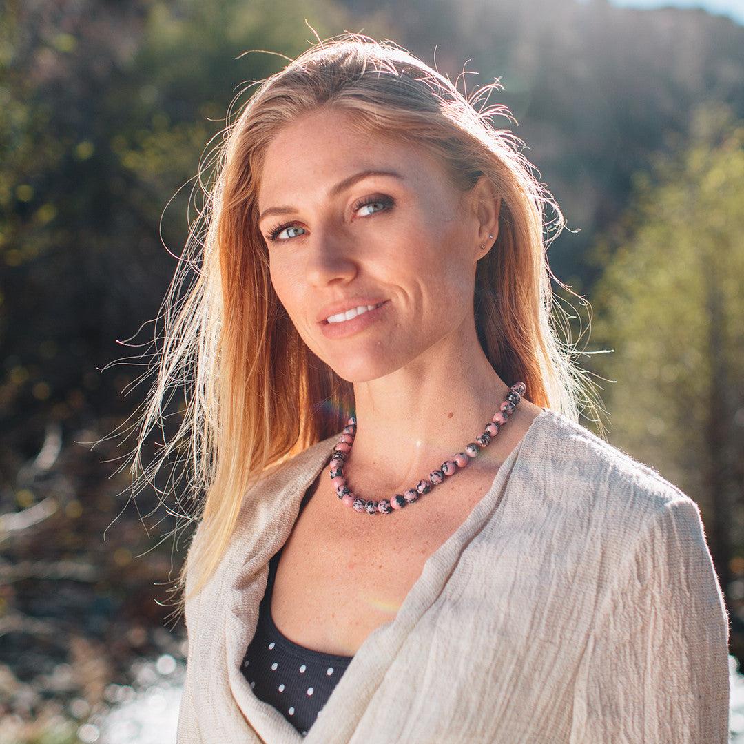 A woman wearing a crystal healing Rhodonite gemstone necklace known for fostering emotional strength and stability