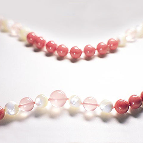 Red and white Radiant Heart therapeutic gemstone necklace displayed on a white table.